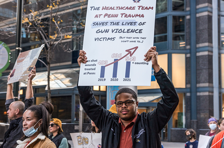 Rodney Babb holds up a sign that says “The Healthcare Team at Penn Trauma Saves the Lives of Gun Violence Victims (but wishes they didn’t have to).”